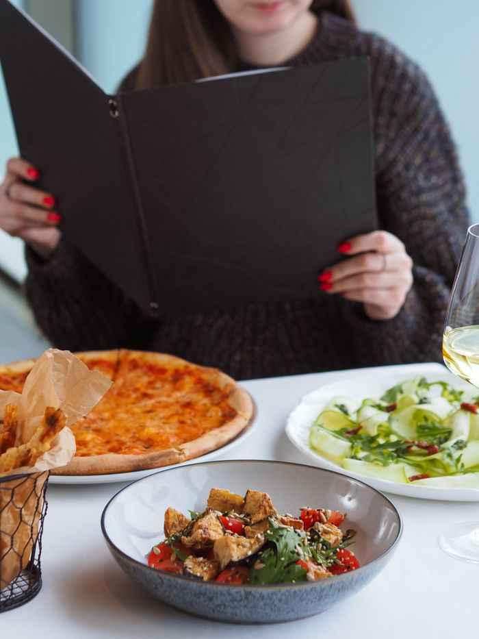 Woman sitting at a restaurant table with pizza, salad, and a menu.