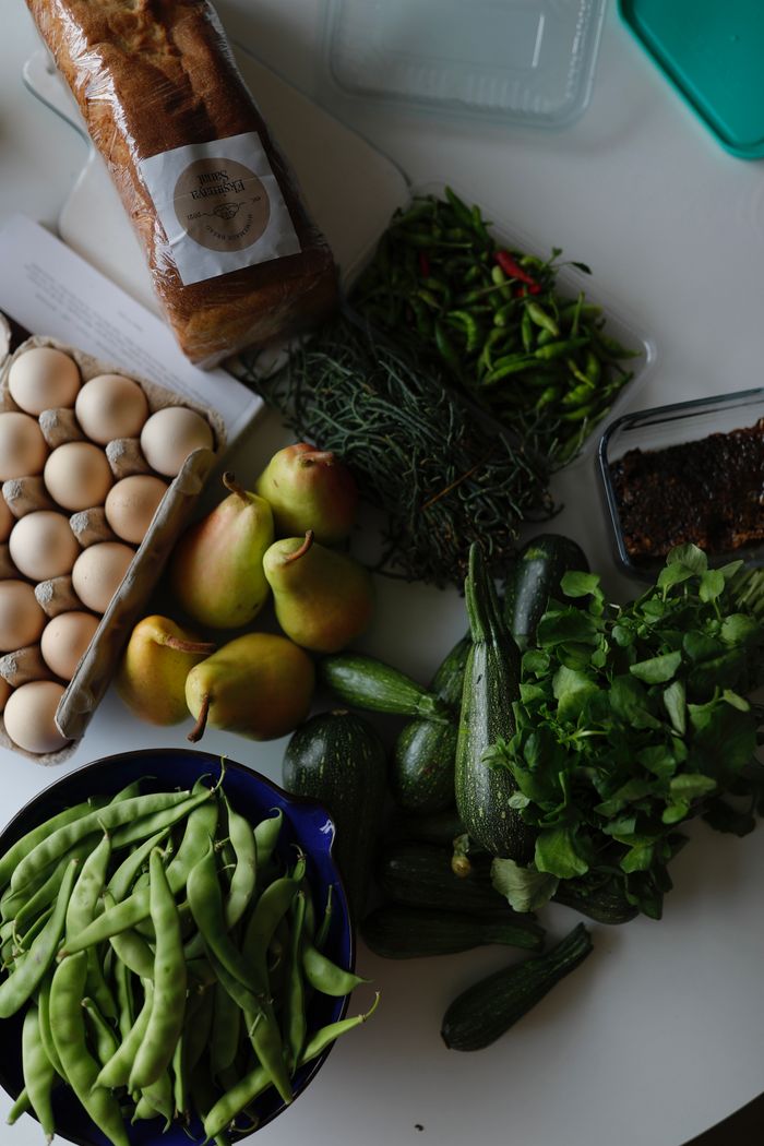 A top view of fresh produce including pears, eggs, and greens on a white table.