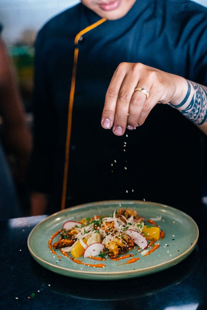 Chef carefully sprinkles sesame seeds on a beautifully plated gourmet dish in a professional kitchen.