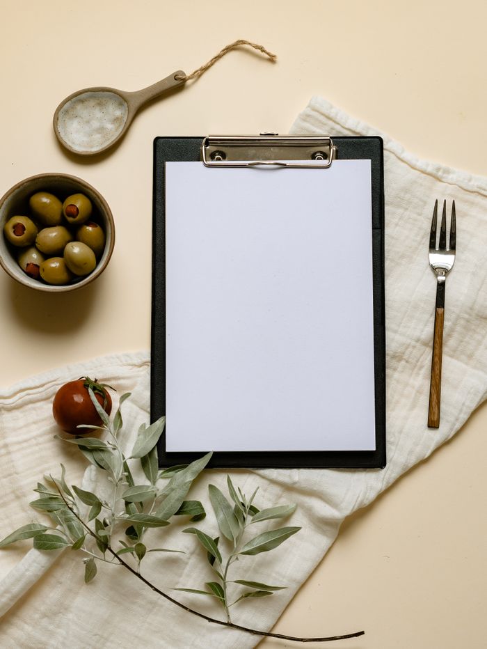 Flat lay of a clipboard, olives, and rustic decor on a beige background.